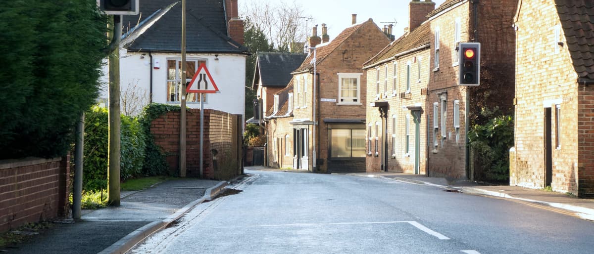 Empty frosted village road at first light, red-brick terraced cottages, Bell Lane sign and a traffic light on red